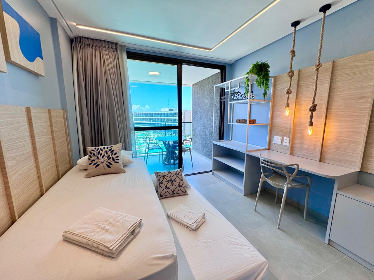 Flat na praia — quarto com marcenaria clara, escrivaninha e vista para varanda